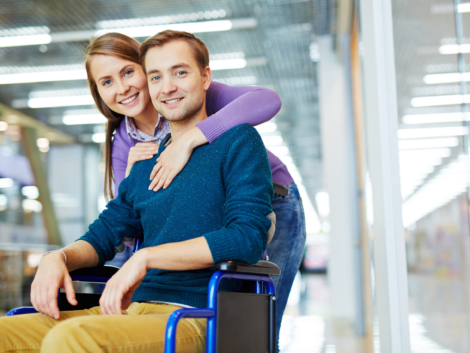 Portrait of young happy couple: pretty girl hugging her smiling handicapped boyfriend in wheelchair